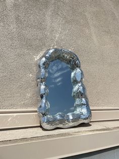 a mirror that is sitting on the side of a building with clouds in the sky