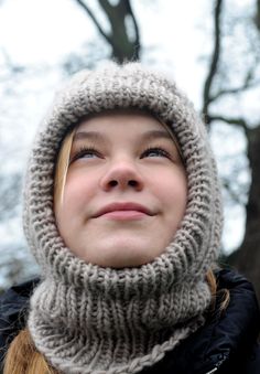 a woman wearing a knitted hat and scarf looks up into the sky with her eyes closed