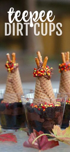 three cones with candy toppings on them are sitting in small cups, surrounded by fall leaves