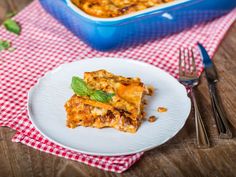 a white plate topped with lasagna next to a blue casserole dish