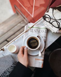 a person sitting at a table with a cup of coffee and newspaper in front of them