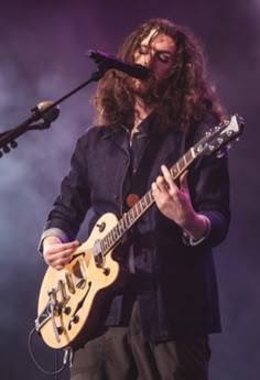 a man with long hair and glasses playing guitar in front of microphones on stage