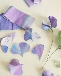 purple and blue paper flowers on a white surface next to green leaves with the word love written on them