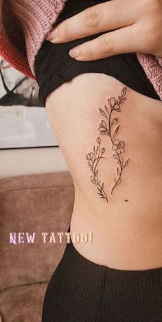 a woman's lower back tattoo with flowers on her stomach and the words new tattoo written in cursive font