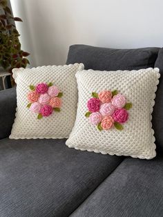 two pillows with pink flowers on them sitting on a couch next to a potted plant