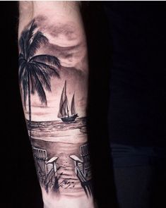 a man's arm with a sailboat and palm trees on the beach at night