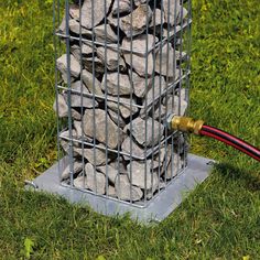 a wire cage filled with rocks sitting on top of a green grass covered field next to a red hose