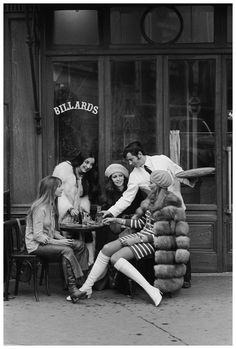 an old black and white photo of people sitting at a table in front of a store