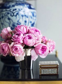 pink flowers are in a silver vase on a table next to an antique box and decorative items