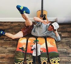 a man laying on the floor with his feet up next to four snowboards and a guitar