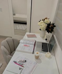 a laptop computer sitting on top of a white table next to a vase with flowers