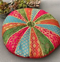 a colorful round pillow sitting on top of a couch next to potted plants and succulents