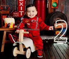 a young boy sitting on top of a wooden toy car in front of a birthday cake