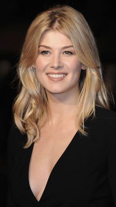 a woman with long blonde hair smiling at the camera and wearing a black dress in front of her