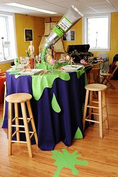 a party table is set up with green and purple decorations on the tablecloths