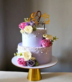 a three tiered cake with purple and yellow flowers on the top is sitting on a gold pedestal