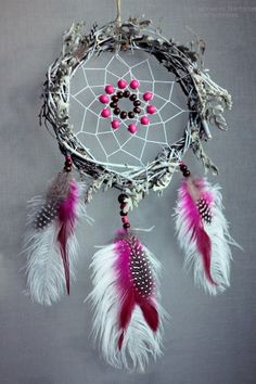 a pink and white dream catcher hanging on a wall next to a gray background with beads