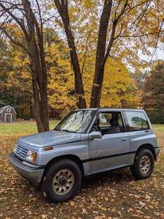 an suv parked in front of some trees with leaves all over the ground and on the ground