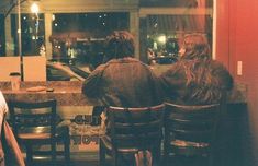 three people sitting at a table in front of a store window with their backs to the camera