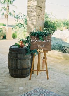 a wooden sign sitting on top of a barrel next to a planter filled with flowers