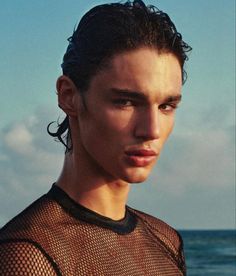 a young man standing on top of a beach next to the ocean wearing a wet suit