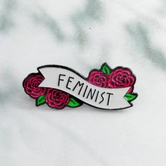 a pin with the word feminist on it and three red roses in front of it