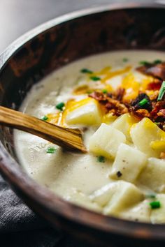 a wooden bowl filled with potatoes and meat on top of a table next to a spoon