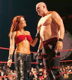 a man and woman standing next to each other in front of a crowd at a wrestling match