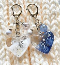 two heart shaped key chains with snowflakes and pearls hanging from them on a white blanket