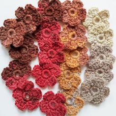 several crocheted flowers are arranged together on a white surface, one is red and the other is brown