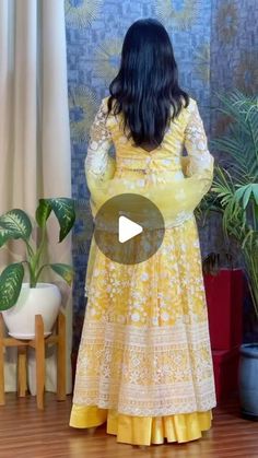 a woman in a yellow dress standing on a wooden floor next to a potted plant