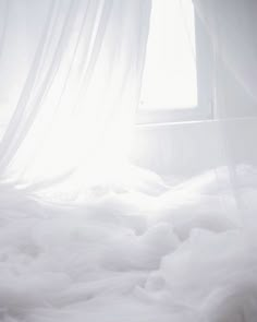 an unmade bed with white sheets and curtains