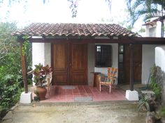 a small house with two chairs and a table in front of the door is surrounded by greenery