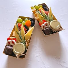 two boxes filled with assorted fruit and cheeses on top of a white table