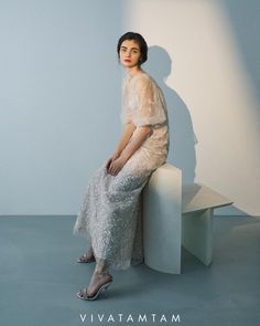 a woman sitting on top of a white bench in front of a light blue wall