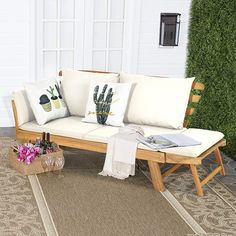 a couch sitting on top of a rug next to a wooden bench with pillows and flowers