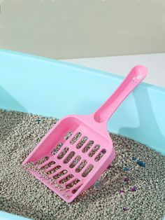 a pink plastic scooper sitting on top of a pile of sand next to a blue bath tub