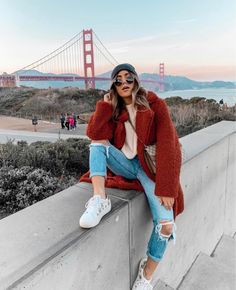 a woman sitting on top of a cement wall next to the golden gate bridge in san francisco