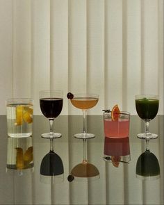 four different types of cocktails sitting on a table with white vertical blinds behind them