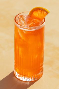 an orange slice is placed on top of a drink in a glass with ice and garnish