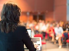 a woman standing in front of an audience with her back to the camera and looking at something