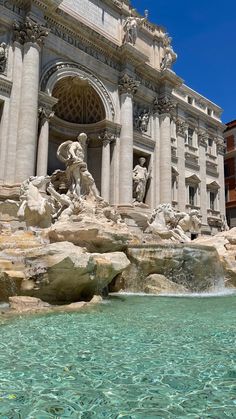 the water is crystal blue and there are many statues in front of this building with columns