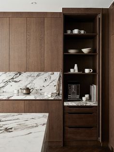 a kitchen with marble counter tops and wooden cabinets, along with white dishes on shelves