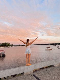 a woman standing on the edge of a pier with her arms in the air