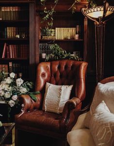 a brown chair sitting in front of a book shelf filled with lots of books and flowers