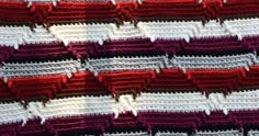 a crocheted blanket with red, white and grey stripes on it's edges