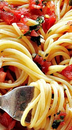 a close up of a plate of pasta with tomatoes and herbs on top, with a spoon in it