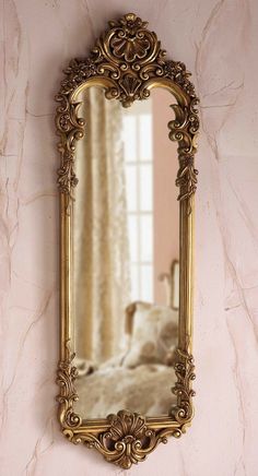 an ornate gold framed mirror on a pink wall