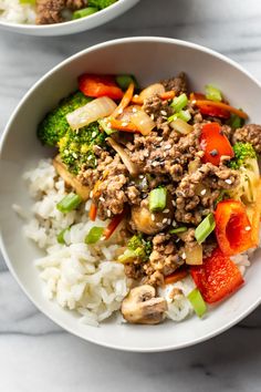 two bowls filled with rice and vegetables on top of a marble countertop next to each other