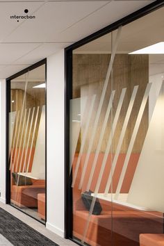 an office with glass walls and orange chairs in front of the windows that have geometric designs on them